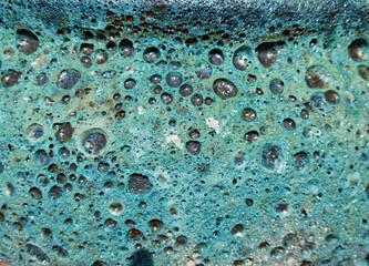 A macro shot reveals an abstract, porous surface with a vibrant turquoise glaze, featuring numerous...
