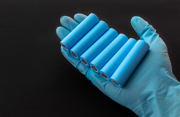 Gloved hand holds blue 18650 lithium-ion battery packs for electrical appliances and devices on black background.