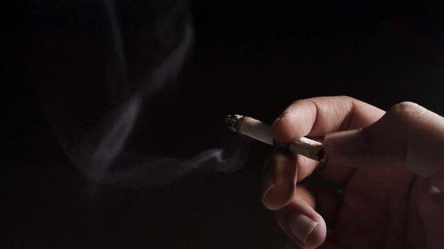 a hand holding a lit cigarette exposed to light against a black background
