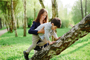 mother and child adventure outdoors. woman supports young boy climbing tree in lush green park....