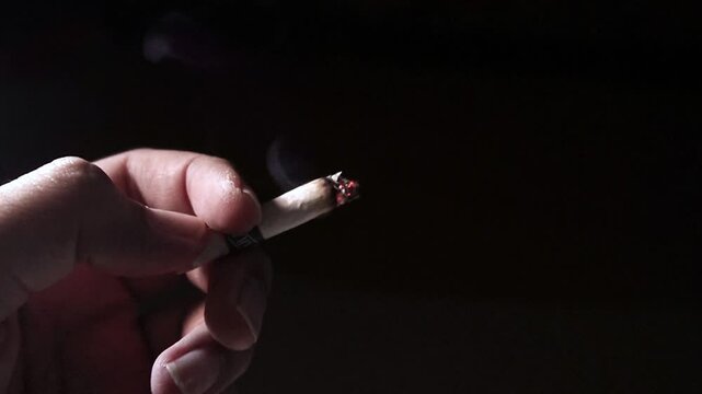 a hand holding a lit cigarette exposed to light against a black background