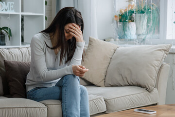 Sad woman sitting on couch with head down and hand covering face