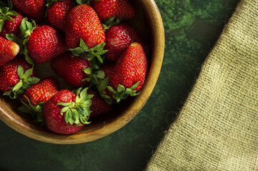 Juicy fresh strawberries from the garden in a wooden bowl on a green background