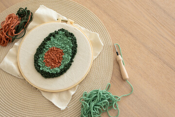 Punch needle embroidery of avocado on hoop. Trendy DIY craft hobby concept, vertical
