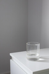 Minimalist glass of water on white bedside table. Mindful living aesthetic, health daily routine habits, vertical