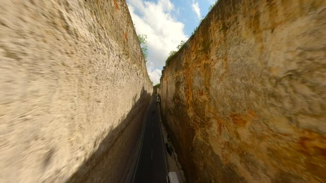 Smooth FPV drone flight over a scenic limestone canyon road at Batu Barak Beach in Bali, Indonesia, showcasing steep cliffs and tropical landscape.