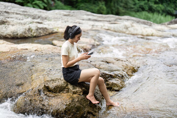 Camping and Nature Connection. Woman relaxing by the river while using her smartphone.