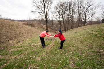 Two individuals engage in a playful tug of war on a grassy hill under overcast skies in a serene...