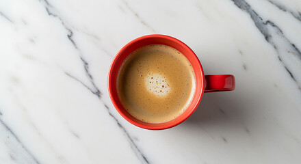 Overhead view of a red mug filled with frothy coffee on a white marble surface