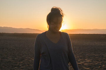 Young woman on the beach at sunset. The sun sets against the sand and trees, and the woman in the...