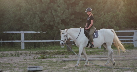 Horseback riding training, young jockey riding white horse in the paddock during golden hour sunset, equestrian sport, active lifestyle, love and care for animals