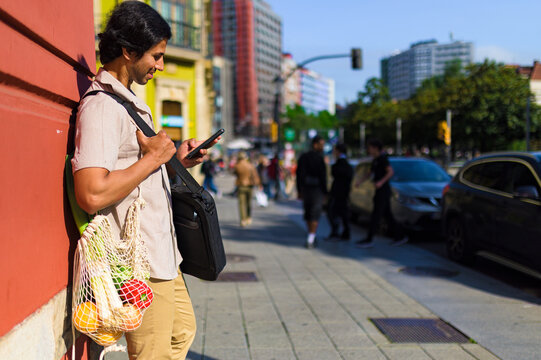 Indian businessman checking his phone while carrying groceries in a reusable bag, promoting sustainability and a healthy lifestyle