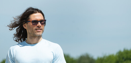 Happy confident man, brunette with long curly hair blowing in wind in sunglasses looking away....