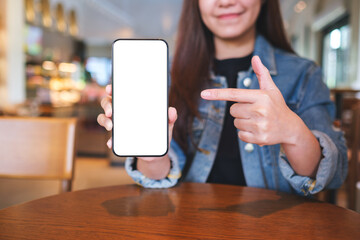Mockup image of a woman holding and pointing finger at a mobile phone with blank white screen in cafe