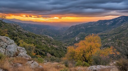 Naklejka premium Dramatic sunset over a mountainous valley, showcasing vibrant autumnal foliage and a cloudy sky