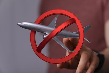 Stock photo of a hand holding a model airplane crossed out by a red circle, symbolizing travel...