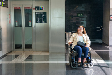 Businesswoman using electric wheelchair waiting for elevator in subway station. Concept of inclusion