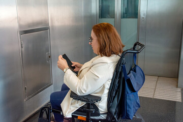 Businesswoman in wheelchair using smartphone in subway station elevator area. Concept of inclusion