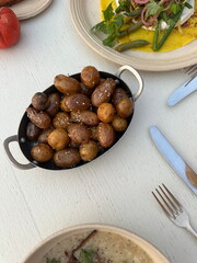 Crispy roasted baby potatoes in a rustic pan, served on a light wooden table with fresh seasonal sides. A cozy outdoor meal in natural daylight, perfect for food lovers and editorial use.