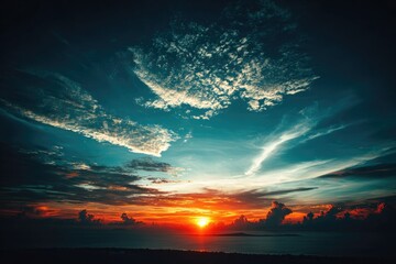 Fototapeta premium Dramatic sunset sky over ocean. Vast expanse of vibrant sunset colors, teal and orange clouds, and a fiery sun sinking below the horizon