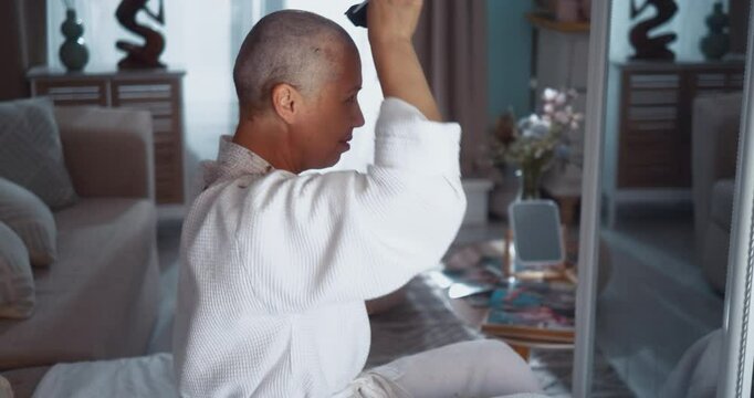 A mature woman with cancer shaves her head with a clipper in front of the mirror at home.