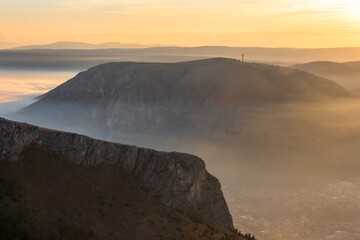 Fog blankets the town of Mostar in Bosnia and Herzegovina at sunset with the outline of a cross is...