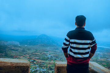 A man gazes at a stunning mountain valley covered in mist. The lush greenery and distant landscape...