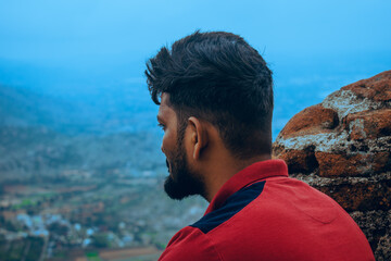  A man in a red t-shirt and sunglasses looks at the scenic valley from an ancient stone viewpoint...