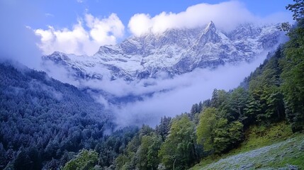 Obraz premium Majestic snow-capped mountains rise above a valley shrouded in mist, with lush green forests clinging to the lower slopes, painted in hues of green and blue under a vibrant sky
