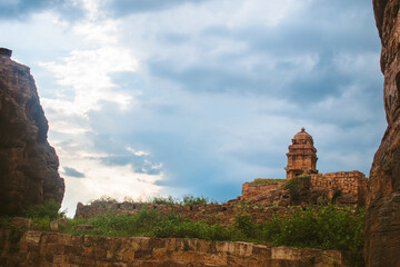 An ancient temple structure partially hidden behind a stone wall under a dramatic monsoon sky in...
