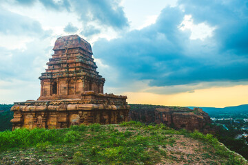 A weathered stone temple(Upper Shivalaya) tower in Badami, Karnataka, stands under a moody sky,...