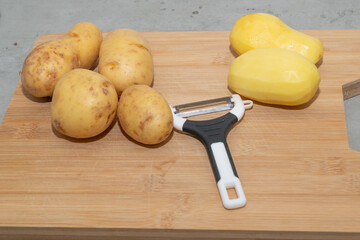 Freshly harvested Potatoes along with a Peeler placed on a rustic Wooden Cutting Board