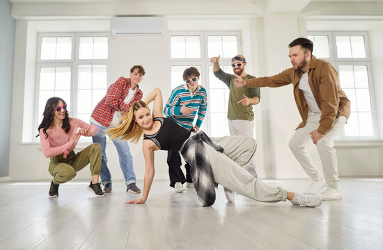 Hip hop dance of young dancers group in studio. Happy students team dancing professional break dance around girl performing creative movement on floor by windows. Choreography class, youth concept - Powered by Adobe