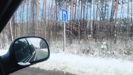 snow-covered road, past trees covered in snow. reflection of winter forest in side view mirror....