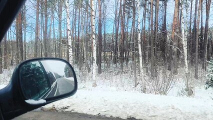 snow-covered road, past trees covered in snow. reflection of winter forest in side view mirror....