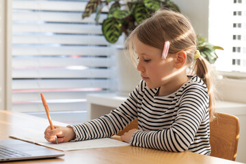 Young girl learning at home with laptop and notebook in bright room. Education concept.