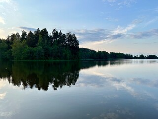 Fototapeta premium Peaceful evening lake reflection, sky and trees silhouettes on the lake surface, summer lake in the countryside