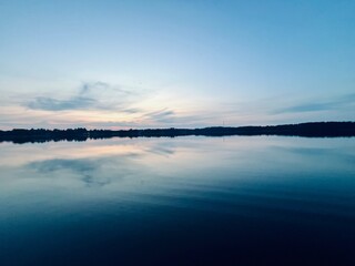 Fototapeta premium Peaceful evening lake reflection, sky and trees silhouettes on the lake surface, summer lake in the countryside