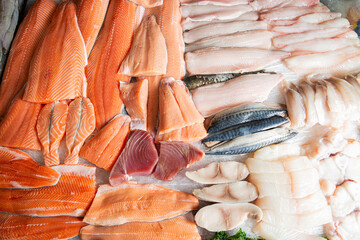 Overhead view of various raw fish fillets - salmon, trout, tuna, mackerel - displayed on a market...