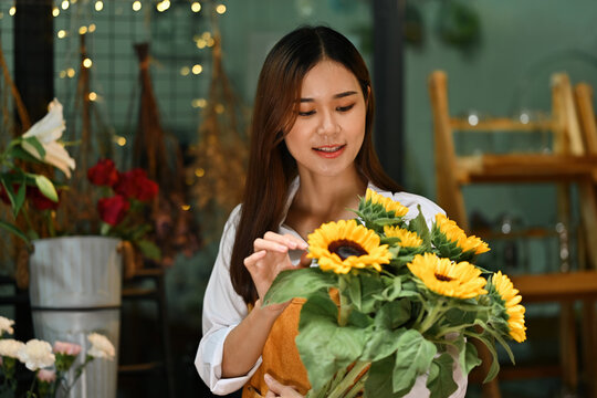 An Asian Female flower shop owner admiring sunflowers while preparing arrangements for her shop display