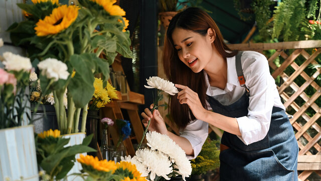 A Young florist arranging white flowers while smiling for display in a vibrant retail setting