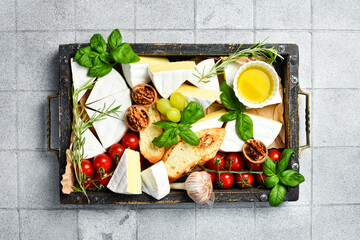 Pieces of Brie cheese, basil, grapes and snacks on a wooden tray. On a stone background.