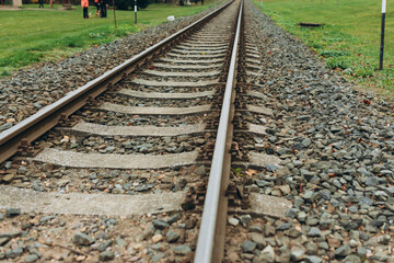Single, diagonal railroad track through countryside landscape with a grass field. Empty railway track. Travel, adventure concept