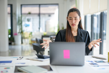 Asian businesswoman showing confused and stressed expression looking at laptop while working on...