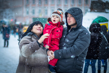 happy family, mom, dad and son near the Christmas tree watching the falling snow