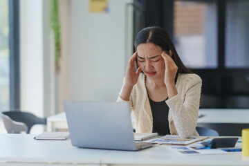 Young office worker suffering from headache while using laptop computer at workplace, feeling tired...