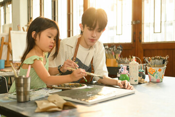 Caring teacher helps a young student explore creativity through hands-on painting activity