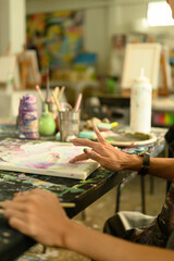 Close-up of an artist's hand using finger painting techniques on a canvas during a creative art...
