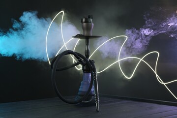 Hookah on wooden table with smoke in color lights against black background