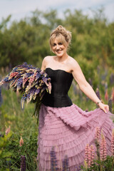 Blonde girl with a bouquet of lupines in a field walking in the summer